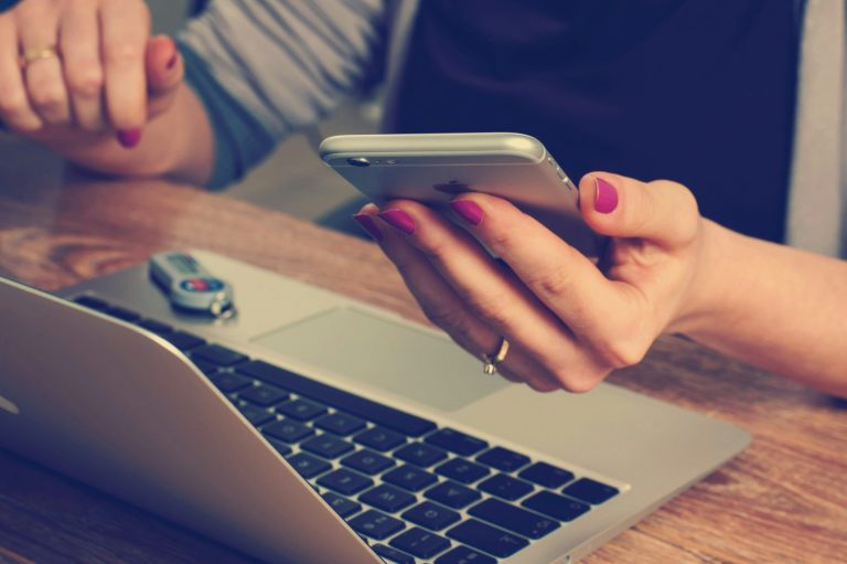 Frau sitzt mit Handy bei Laptop