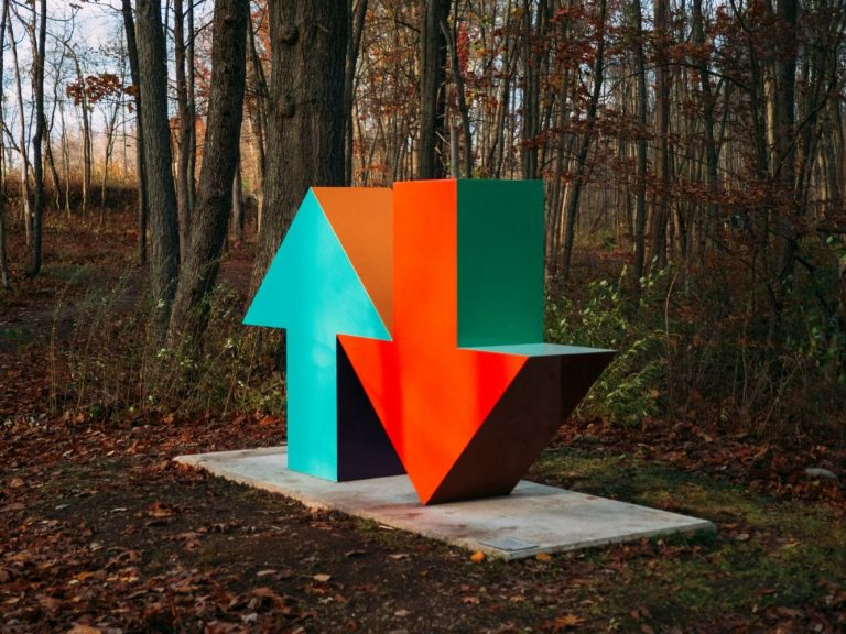 Eine Skulptur im Wald, von einem blauen Pfeil nach oben und einem roten Pfeil nach unten